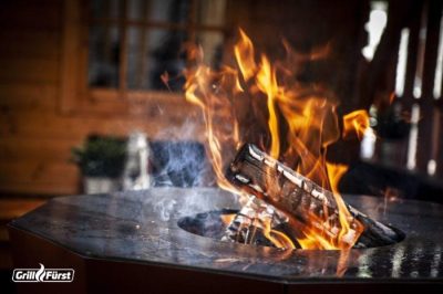 Brennende Holzscheite in der Mittelöffnung einer Feuerplatte