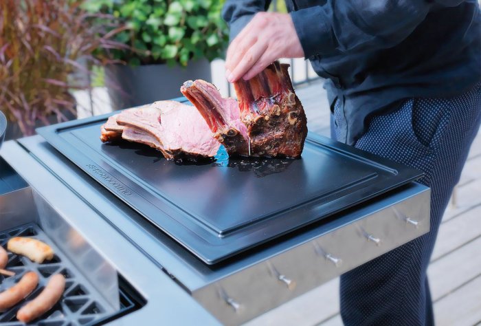 Großes schwarzes Kunststoff-Schneidebrett auf einer Grill-Seitenablage mit tranchiertem Fleisch